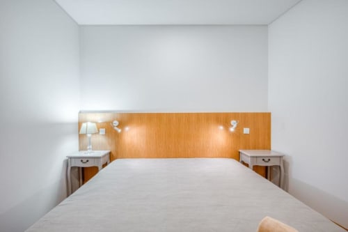 Quarto moderno e luminoso com paredes brancas, cabeceira de madeira, mesas de cabeceira gêmeas e luminária no apartamento Villa Amore com vista para o mar em Paul