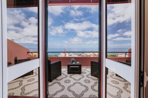 Varanda privada da Villa Amore com vista para o oceano, cadeiras pretas, paredes em terracota e paisagem costeira
