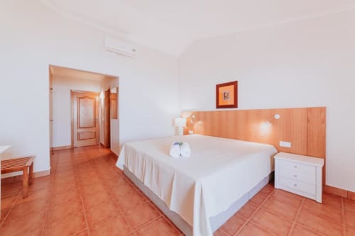 Quarto espaçoso com cama de casal, cabeceira de madeira, piso em terracota e vista para o oceano na Villa Amore, Portugal