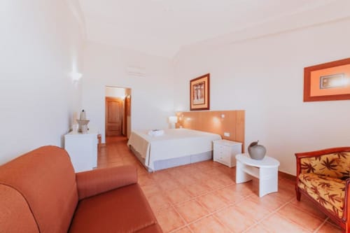 Amplo quarto de casal na Villa Amore com azulejos em terracota, detalhes em madeira alaranjada, área de estar com sofá e comodidades modernas