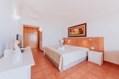 Espaçoso quarto de casal com piso de cerâmica terracota, paredes brancas, cabeceira de madeira e comodidades modernas na Villa Amore