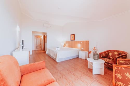 Suíte espaçosa na Villa Amore com piso em terracota, cama branca, móveis laranja e vista para o mar