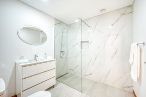 Banheiro moderno na Villa Amore com chuveiro de mármore, espelho oval, pia branca e toalheiro aquecido no apartamento de Paul do Mar.