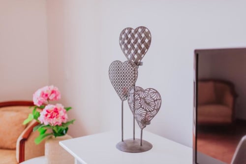 Esculturas decorativas de corações em metal sobre mesa no quarto de hóspedes Villa Amore, com flores rosas e vista para o oceano