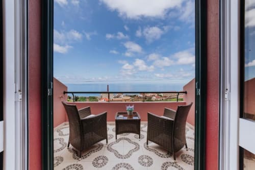 Terraço privado da Villa Amore com móveis de vime, vista para o oceano e jardim sob céu azul