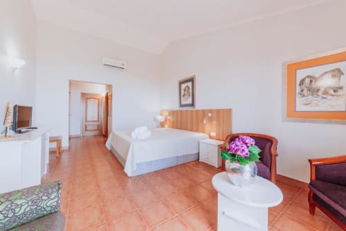 Espaçoso quarto duplo na Villa Amore com cama branca, pisos em azulejo de terracota, cabeceira de madeira e obra de arte com vista para o oceano