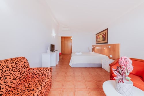 Espaçoso quarto duplo na Villa Amore com assentos padrão laranja, cama branca, piso em terracota e vista para o mar