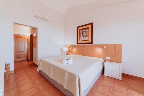 Espaçoso quarto de casal com piso de ladrilho terracota, roupa de cama branca, cabeceira de madeira e comodidades modernas na Villa Amore,