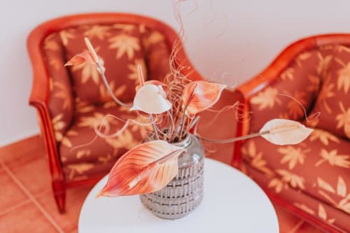 Decoração elegante na Villa Amore com poltronas estampadas em coral, mesa branca e arranjo de flores secas em vaso de vidro.