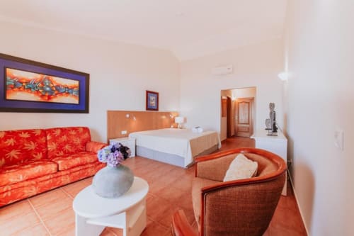 Suíte espaçosa da Villa Amore com sofá estampado vermelho, piso em terracota, cama com vista para o oceano e design contemporâneo