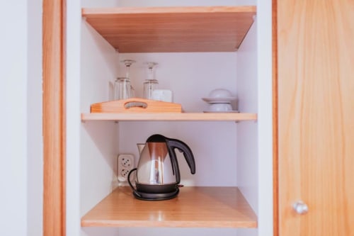 Armário de cozinha na Villa Amore B&B com chaleira elétrica, copos e prateleiras de madeira