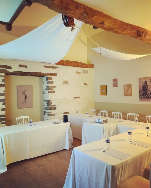 Conference room at Manoir de la Bégaudière with rustic wooden beams, exposed brick, white linens, and cream walls