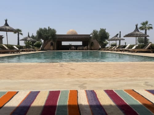 La piscine luxueuse de la Villa Rêve D'ahlam avec chaises longues rayées, parasols en chaume et architecture marocaine à Jbilate