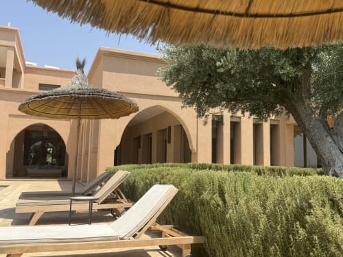 Coin lounge dans la cour de Villa Rêve D'ahlam avec parasol de chaume, transats en bois et architecture méditerranéenne