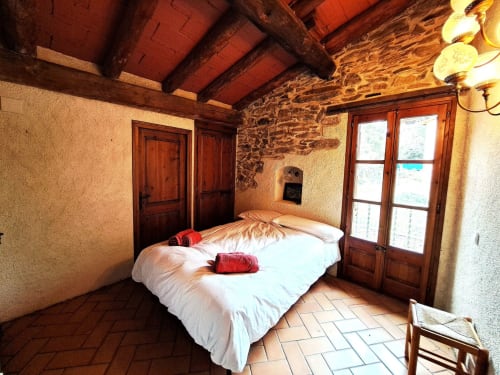 Dormitorio rústico de piedra en L'Orri Rectoria Nova en Campelles con vigas de madera, cama blanca y vistas a las montañas