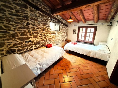 Amplio dormitorio de piedra en L'Orri Rectoria Nova con dos camas, suelo de barro cocido, vigas de madera y vistas a la montaña