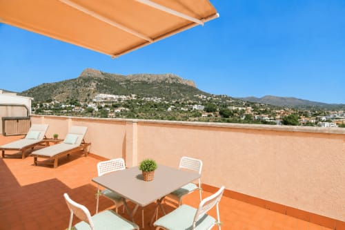 Terraza de la azotea de Riurau Home en Calpe con vistas a la montaña, tumbonas, mesa de comedor y toldo naranja