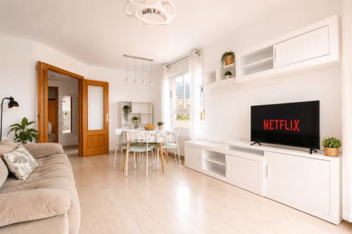Apartamento moderno diáfano en Calpe con sofá beige, mueble blanco con Netflix en TV, comedor, puertas de madera