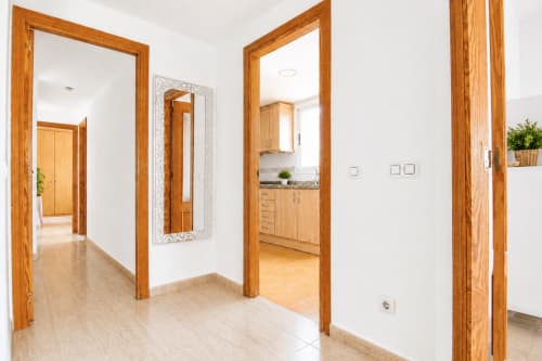 Pasillo luminoso con marcos de puerta de madera en el apartamento Riurau Home de Calpe, que conduce a la cocina y las habitaciones