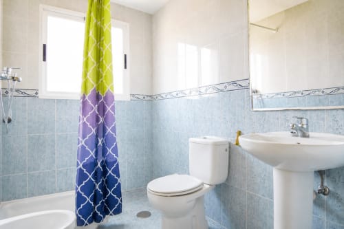 Baño moderno en Riurau Home, Calpe, con azulejos azules, lavamanos blanco, inodoro y cortina de ducha colorida