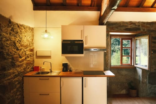 Cocina moderna en el Apartamento Cerezos de Casa Grande de Covas, Taboada con armarios color crema, encimeras de madera y muros de piedra