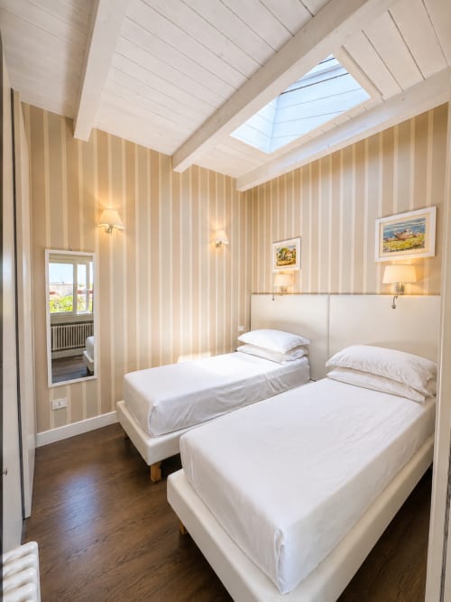 Camera da letto luminosa in soffitta presso il B&B Pellicano a Reggio Calabria con due letti, lucernari, pareti a righe e accesso alla vista mare