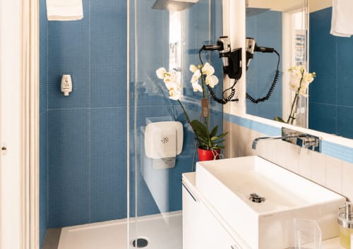 Bagno moderno presso B&B Pellicano con piastrelle blu, lavabo bianco, doccia in vetro e orchidee bianche in vaso rosso