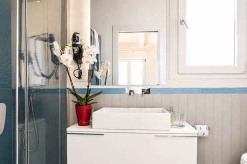 Bagno moderno al B&B Pellicano con lavabo rettangolare bianco, accenti in piastrelle blu, orchidee bianche e soffione pioggia
