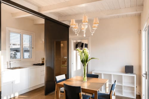 Zona pranzo moderna con tavolo in legno, sedie blu, scaffalature bianche e elegante lampadario nell'appartamento B&B di Reggio Calabria