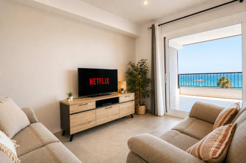 Salón moderno con vistas al mar en Riurau Home, Calpe. Sofás beige, TV de pantalla plana y balcón con vistas