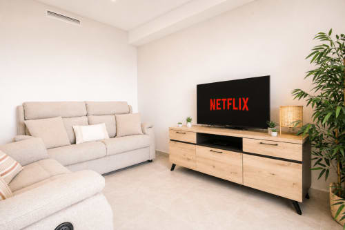 Moderna sala de estar del apartamento Riurau Home Calpe con sofá beige, mueble de madera para TV y Netflix en pantalla plana