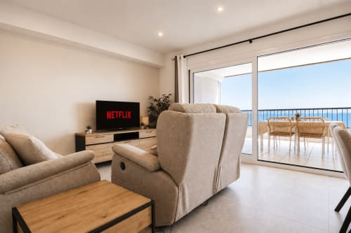 Moderno salón en Riurau Home Calpe con muebles beige, televisor, balcón con vistas al mar y comedor con vista a la costa.