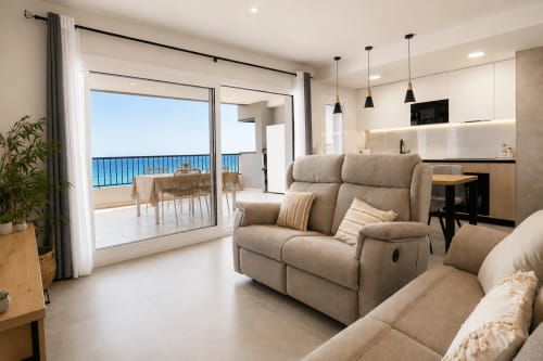 Moderno apartamento en primera línea de playa de Calpe con vistas al mar, cómodo sofá beige, cocina equipada y terraza con vistas