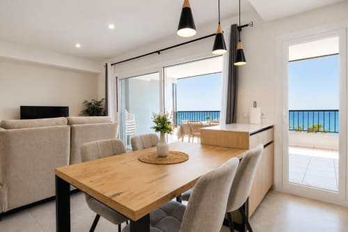 Zona de comedor y salón diáfana con vistas al mar, mesa de madera y balcón costero en Riurau Home Calpe