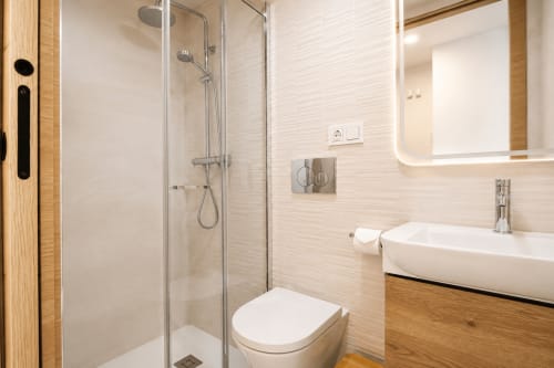 Baño moderno en apartamento Riurau Home Calpe con ducha a ras de suelo, lavabo blanco, inodoro y espejo iluminado
