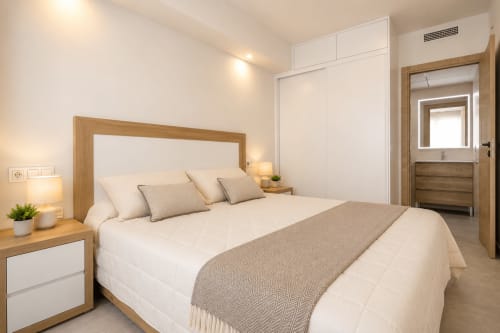Moderno dormitorio en Riurau Home Calpe con ropa de cama blanca, cabecero de madera, armario empotrado y baño privado con vistas al mar
