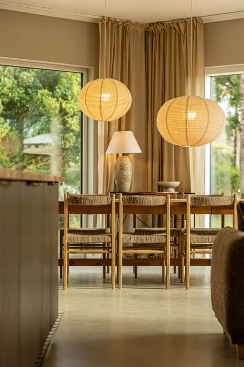 Modern dining room at Sea'Ya Casa Pavão villa with wooden chairs, pendant lanterns, and garden views through large windows