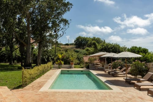 Sea'Ya Casa Pavão villa pool in Colares with loungers, umbrellas, terrace, and lush gardens under blue sky
