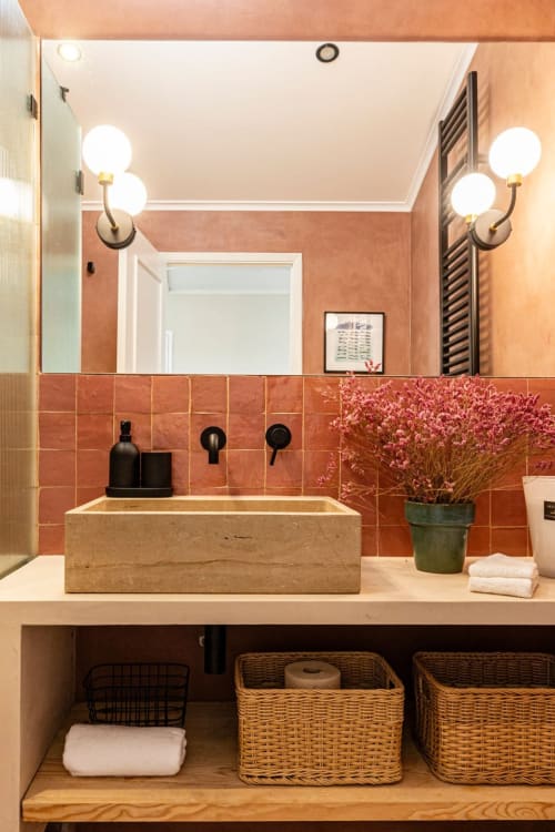 Modern bathroom at Sea'Ya Casa Pavão villa in Colares with terracotta tiles, stone sink, dual sconces, and woven storage