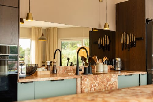 Modern kitchen with coral granite countertops, mint cabinets, and brass pendant lights at Sea'Ya Casa Pavão villa in Colares