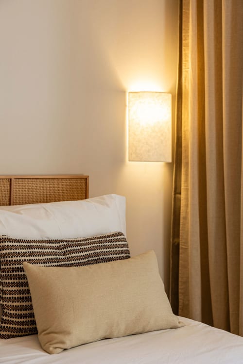 Modern bedroom at Sea'Ya Casa Pavão villa with rattan headboard, cream bedding, decorative pillows, and warm wall sconce