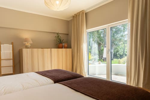 Bright bedroom in Sea'Ya Casa Pavão villa, Colares, with twin beds, wooden headboard, and glass doors opening to garden view