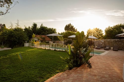 Sunset view of Sea'Ya Casa Pavão villa's terrace with brick patio, manicured lawn, pool area, stone walls, and lounge chairs