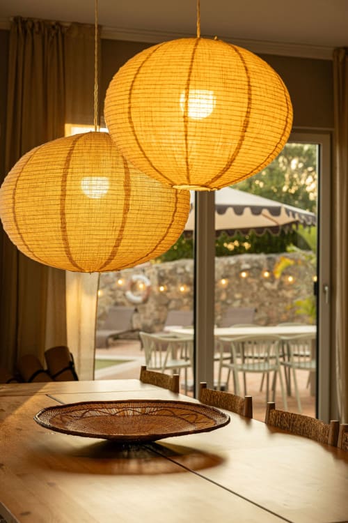 Two golden woven pendant lanterns hang above a dining table at Sea'Ya Casa Pavão villa in Colares, with pool view terrace