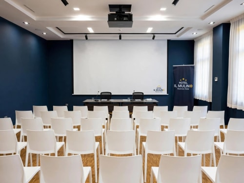 Sala conferenze moderna dell'Hotel Il Mulino con sedie bianche, pavimento in legno, schermo di proiezione e pareti blu scuro