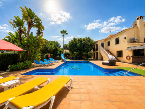 Sunny pool area at Casa Emilia villa in Moraira with blue swimming pool, yellow loungers, palm trees, and beige