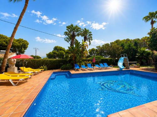 Crystal blue swimming pool with lounge chairs, slide, and palm trees at Casa Emilia villa in Moraira