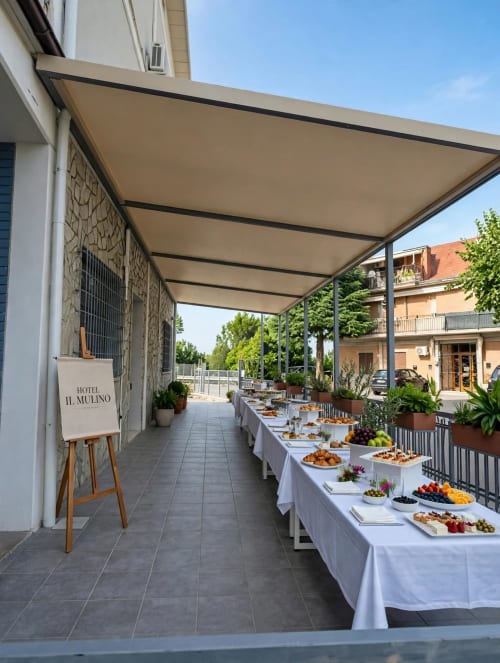 Terrazza esterna dell'Hotel Il Mulino con allestimento buffet, tovaglie bianche, frutta fresca sotto la tenda beige