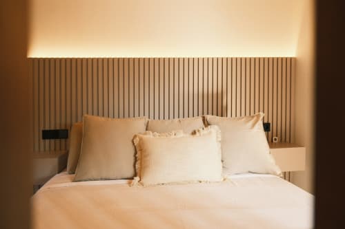 Dormitorio minimalista en Casa Grande de Covas, Taboada, con ropa de cama crema, almohadas neutras y cabecero de lamas de madera vertical