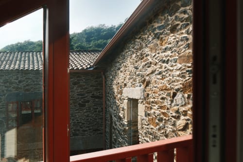 Arcada de piedra con viga roja en Casa Grande de Covas, Taboada, mostrando arquitectura rústica y vista de bosque en ladera